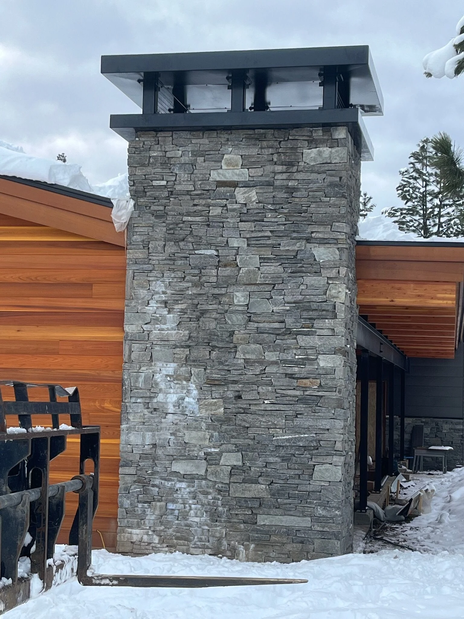 custom black metal chimney cap on stacked stone chimney
