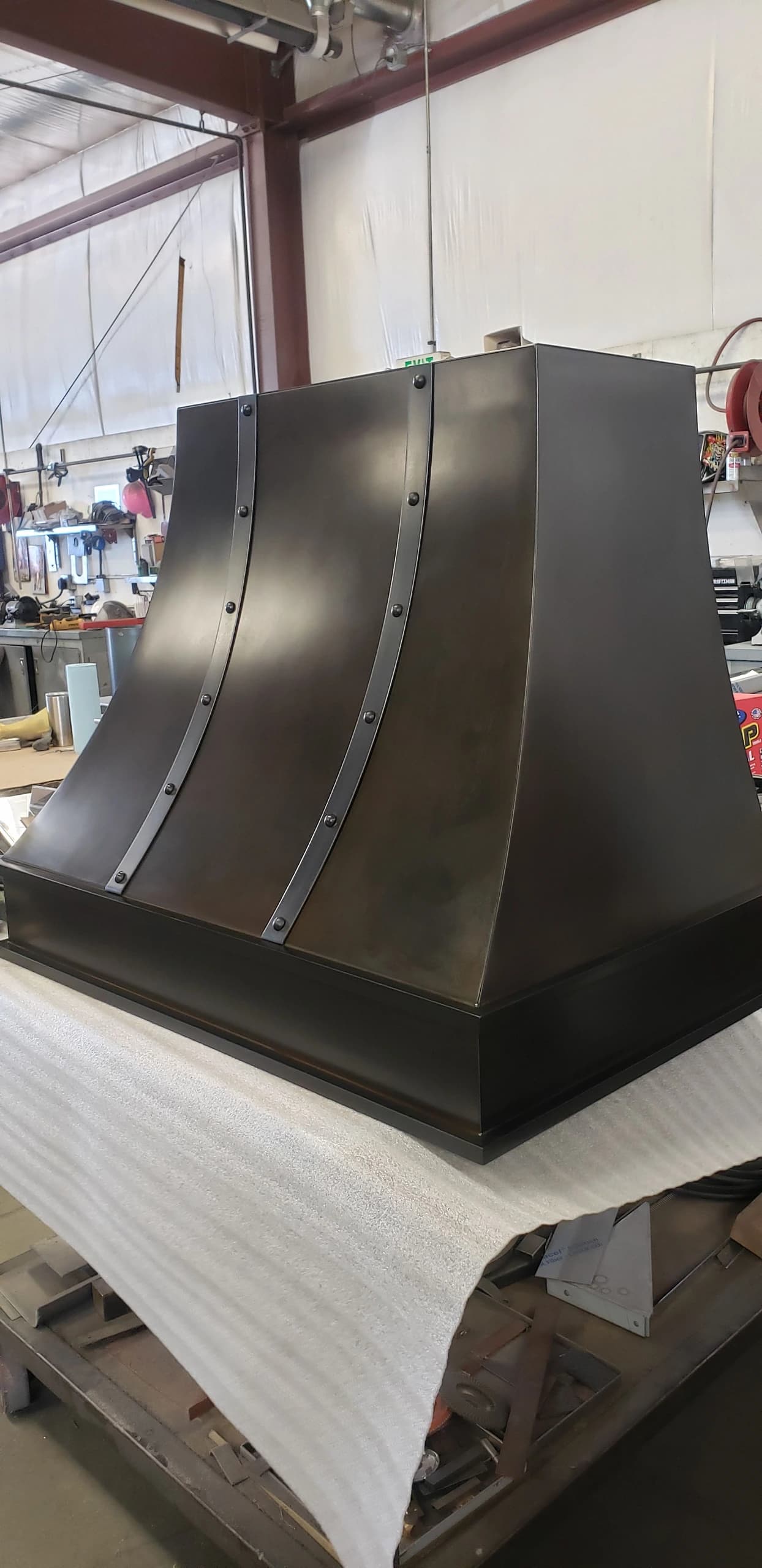 dark custom range hood rivets on industrial fabrication shop bench