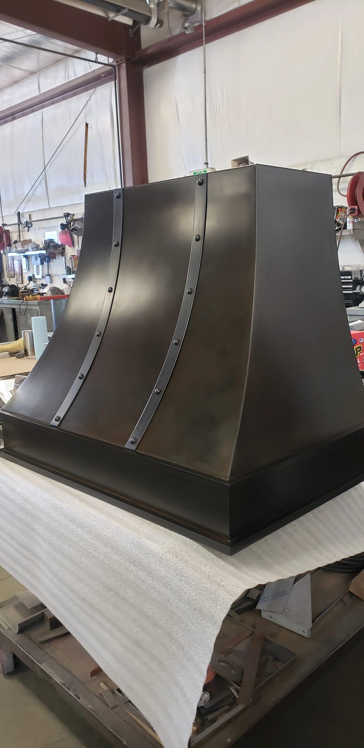 dark custom range hood rivets on industrial fabrication shop bench